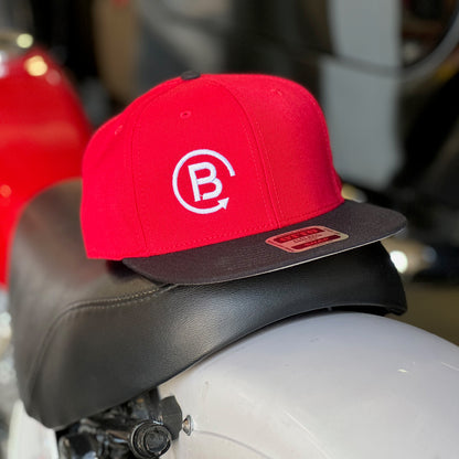 Red embroidered ball cap with black brim sitting on a dirt bike seat.