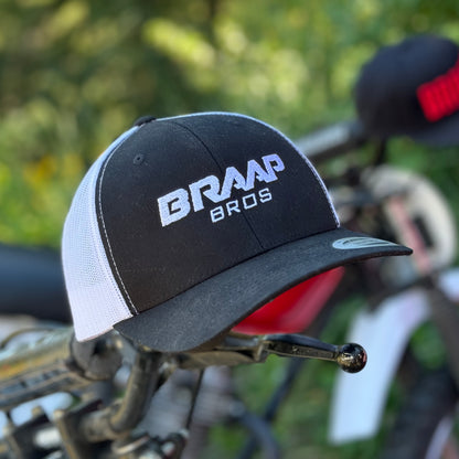 Braap Bros. trucker hat on handlebars of a dirtbike in the mountains.